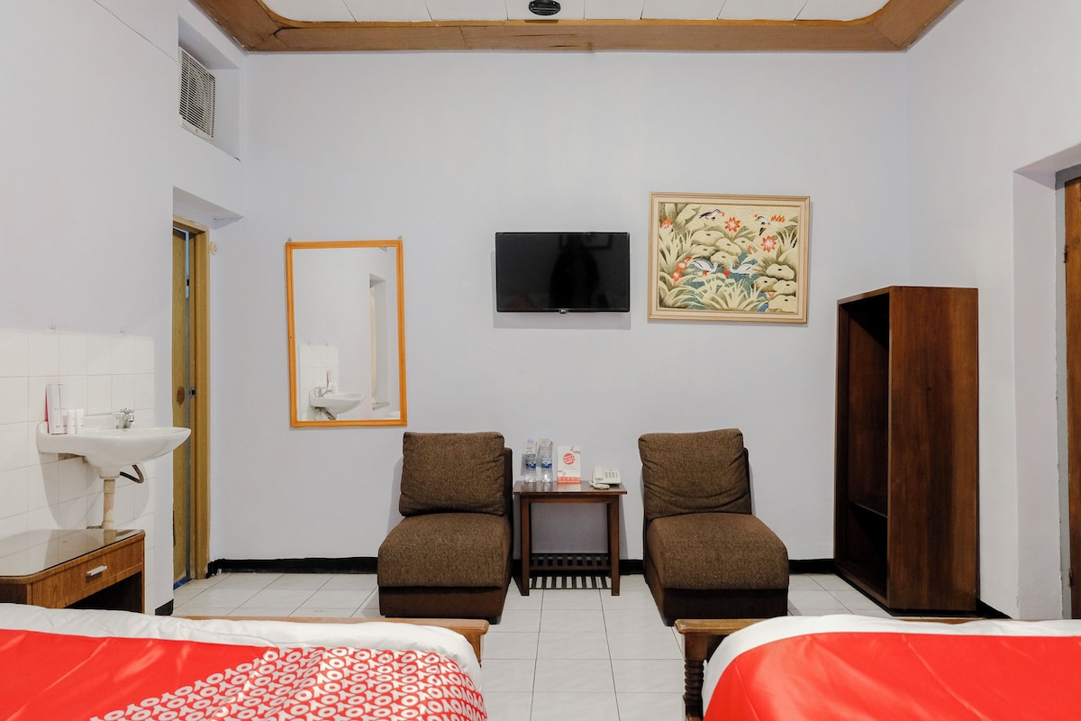 Une chambre d’hôtel avec deux lits, une télévision, un tableau, une armoire et une petite table avec des articles de toilette.