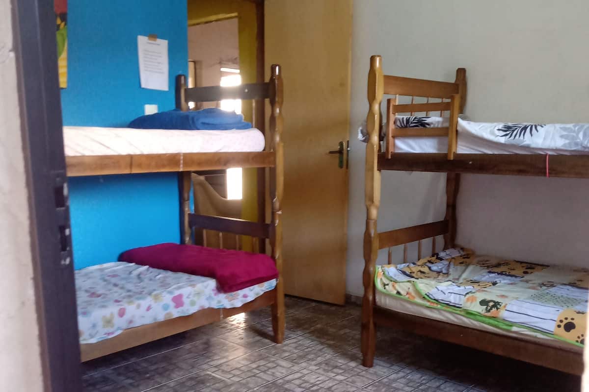 A dormitory room with two bunk beds, a small stool, and a door leading to another room.