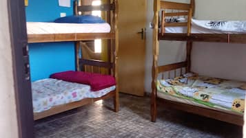 A dormitory room with two bunk beds, a small stool, and a door leading to another room.