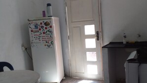 A kitchen with a white refrigerator covered in magnets and notes, a white door with a window, and a small countertop with a sink and a bottle.