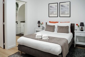 A neatly made bed with two towels, a bedside table with a lamp, and a nightstand with a lamp. There are two framed pictures on the wall above the bed. - Porto Ribeira Studio Apartment - Rio Douro  (Porto)
