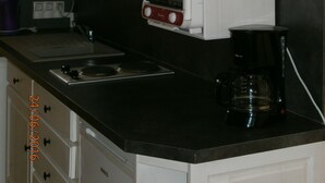 A kitchen with white cabinets, a black countertop, a stove, and a coffee maker. - Gite Valley of Seine, located in Lillebonne Roman city (LILLEBONNE)