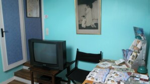 A room with a television on a wooden stand, a chair, a table with magazines, and a framed picture on the wall. - Gite Valley of Seine, located in Lillebonne Roman city (LILLEBONNE)
