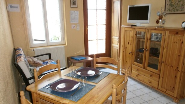 A dining area with a wooden table set for four, a television on a cabinet, and a window with blinds. - Gite Valley of Seine, located in Lillebonne Roman city (LILLEBONNE)