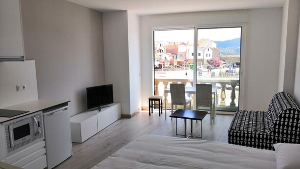 A modern hotel room with a balcony, a flat-screen TV, a dining table, and a sofa. - Studio with sea views (APT 1) (Combarro)