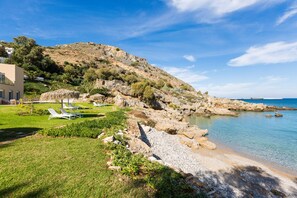 A coastal property with a grassy area, lounge chairs, and a rocky shoreline.