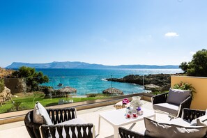 A balcony with wicker furniture, a table, and a view of the sea and mountains.