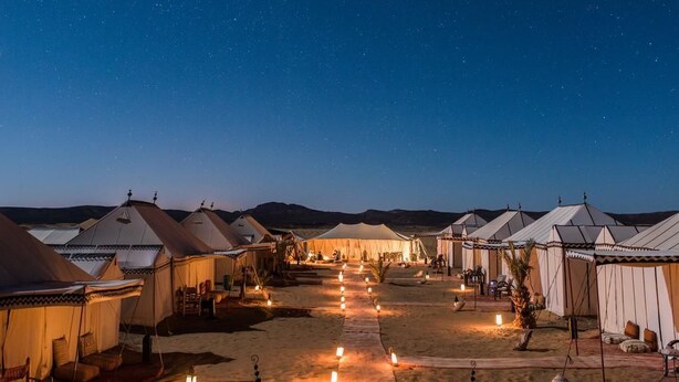 A series of tents arranged in rows with a central walkway, under a starry night sky. - Bedouin Tent Merzouga (Taouz)