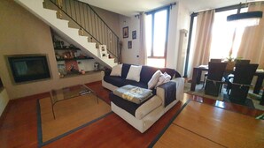 A living room with a sofa, a coffee table, a TV, a staircase, and a dining area with chairs and a table.
