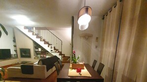 A dining area with a wooden table, chairs, a vase with flowers, and a staircase leading to an upper level.