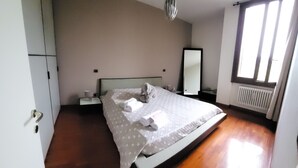 A bedroom with a bed, a nightstand, a mirror, and a window.