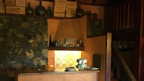 A rustic interior with stone walls, a wooden ceiling, and a bar area with bottles and boxes. There are two white armchairs with patterned cushions. - Finca la Chirita - For hikers, starry nights (Icod de los Vinos)