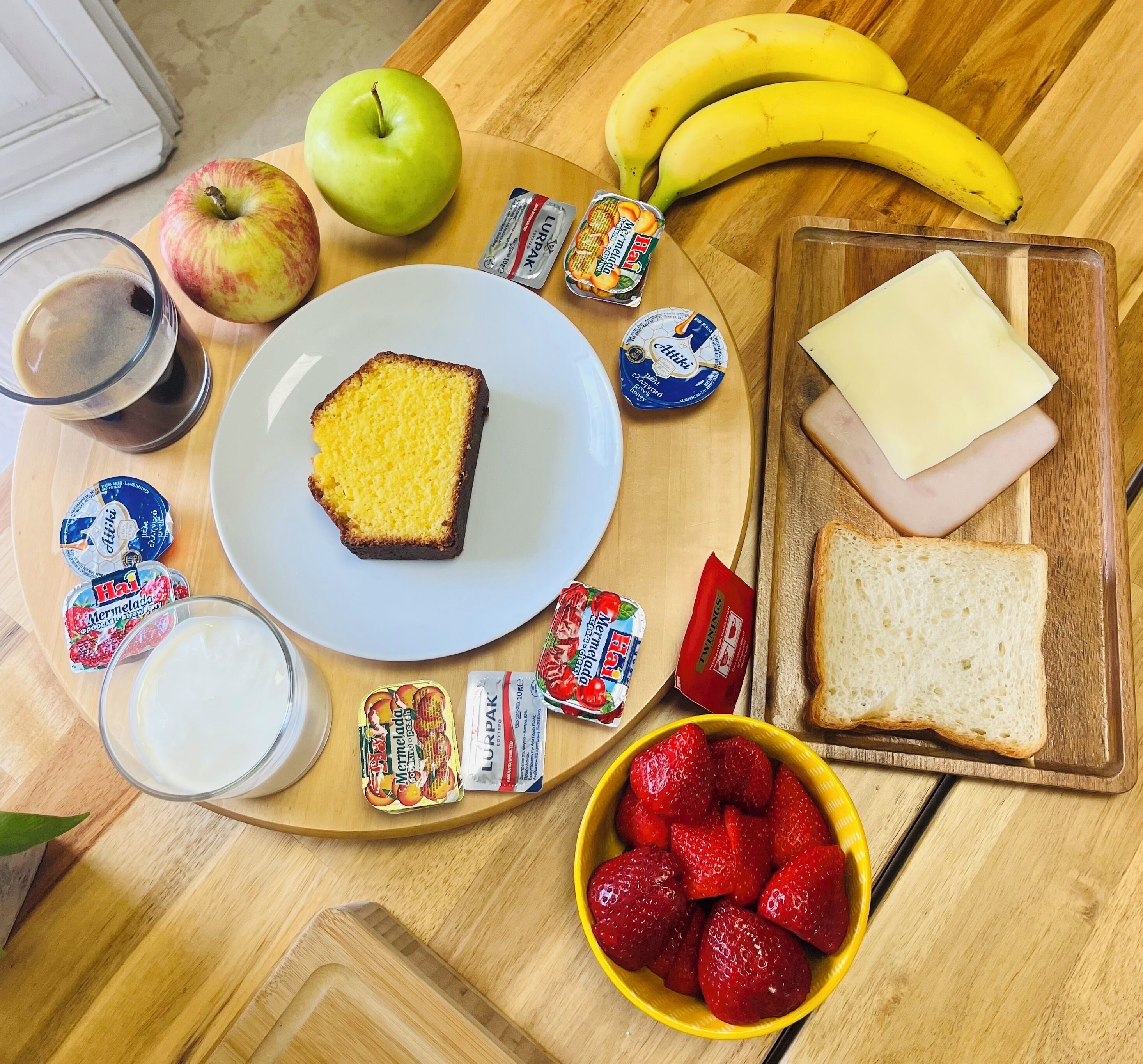 A breakfast tray with toast, cheese, strawberries, a banana, an apple, and various spreads.
