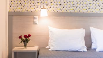 Una cama bien tendida con almohadas blancas, una mesita de noche con un jarrón de rosas rojas y una pared con un diseño geométrico.