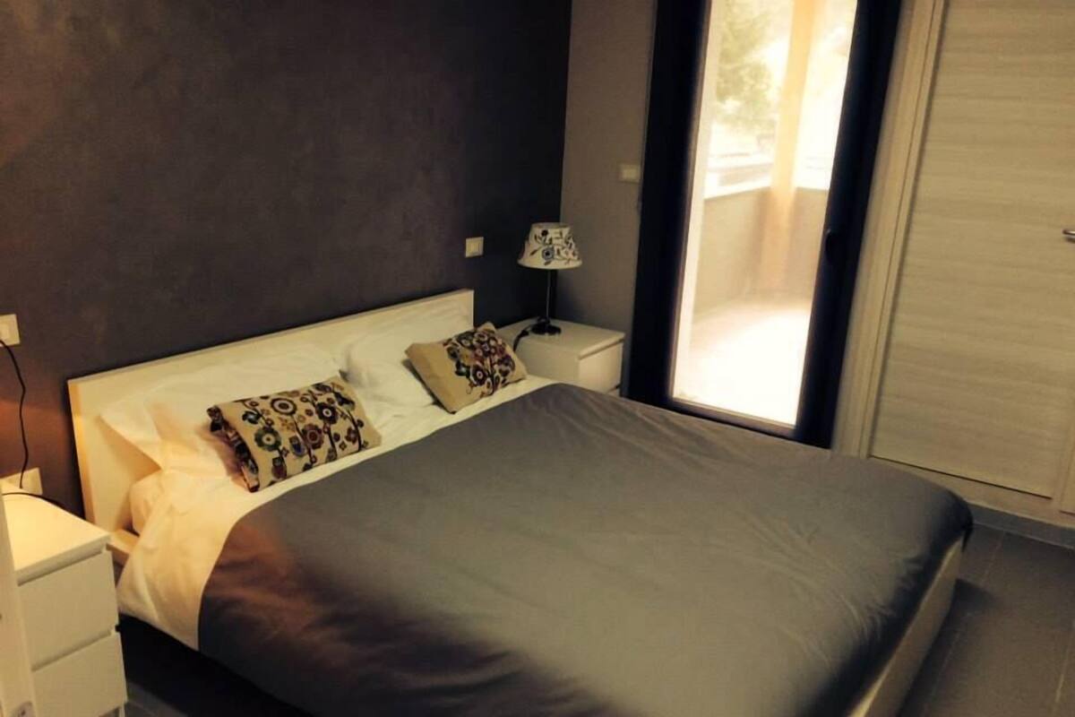 A modern bedroom with a large bed, two bedside tables, a nightstand, and a window with curtains.