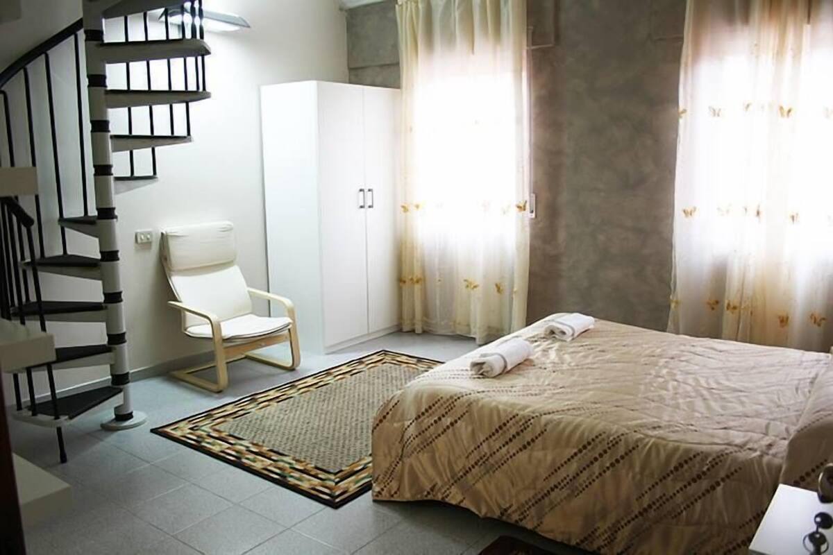 A bedroom with a bed, a chair, a wardrobe, and a spiral staircase.