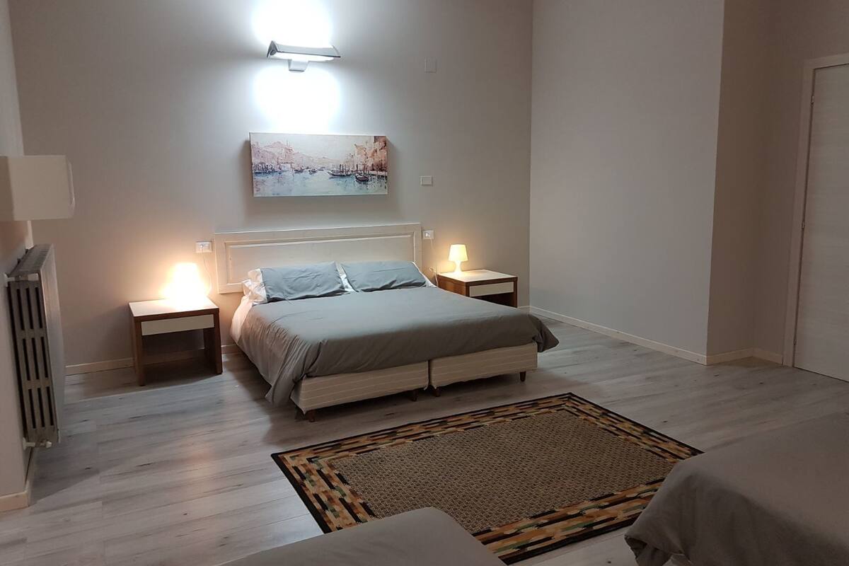 A bedroom with a bed, bedside lamps, a painting, and a radiator.
