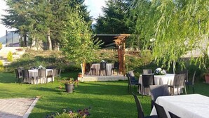 Une terrasse extérieure avec des tables et des chaises, entourée de verdure et agrémentée d’une pergola.