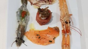 Une assiette carrée contenant divers fruits de mer, notamment des crevettes, un morceau de poisson et un filet de saumon.