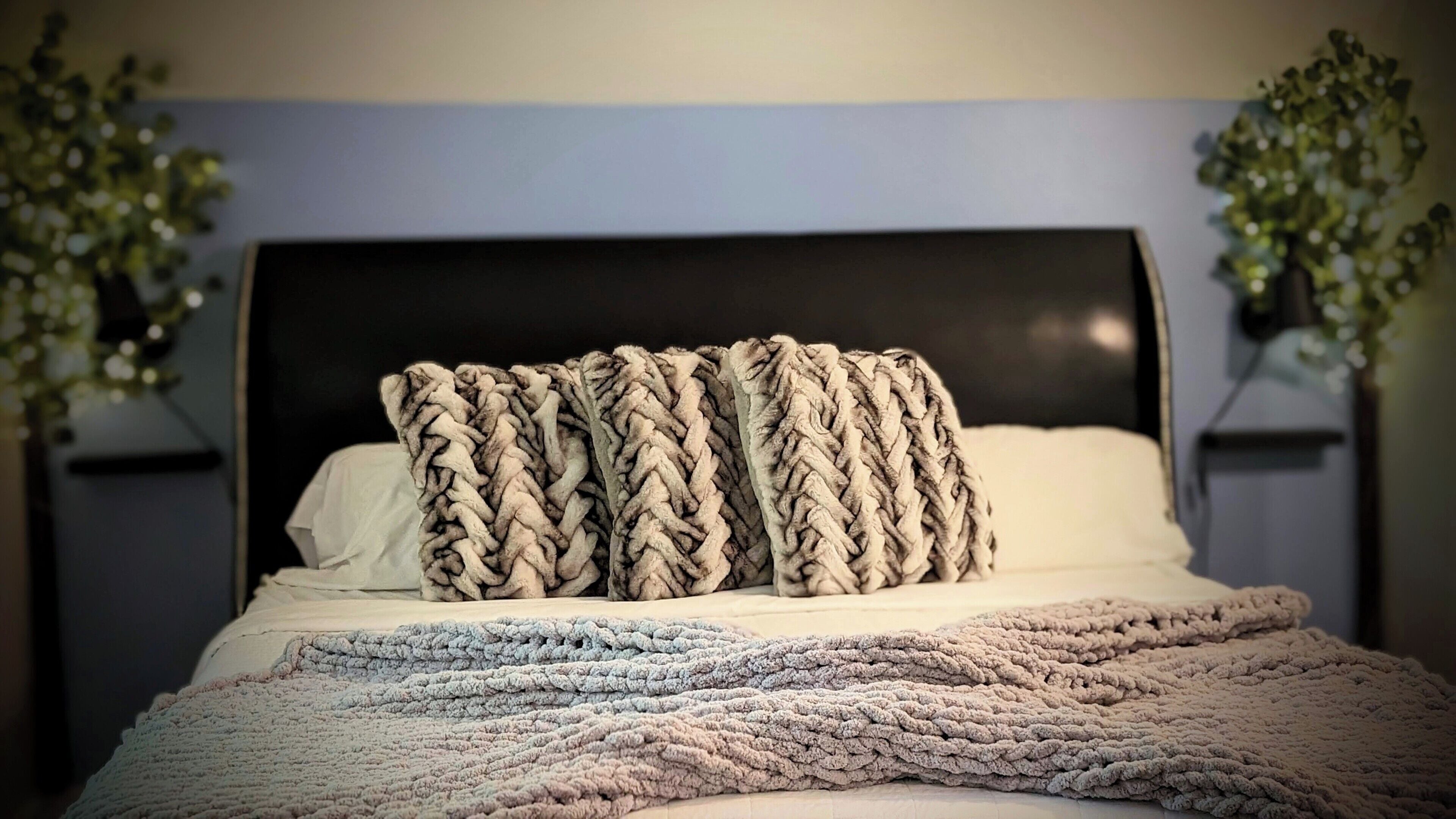 Una cama con un plaid tejido, almohadas y un cabecero oscuro.