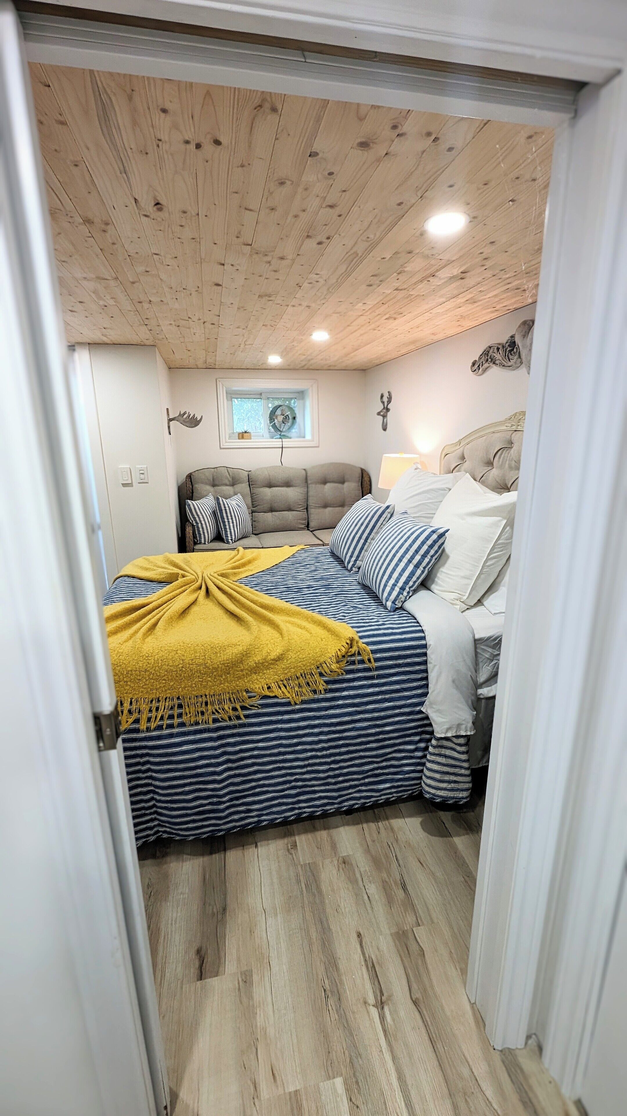A bedroom with a wooden ceiling, a bed with striped bedding, a yellow throw blanket, and a headboard with a decorative headpiece.