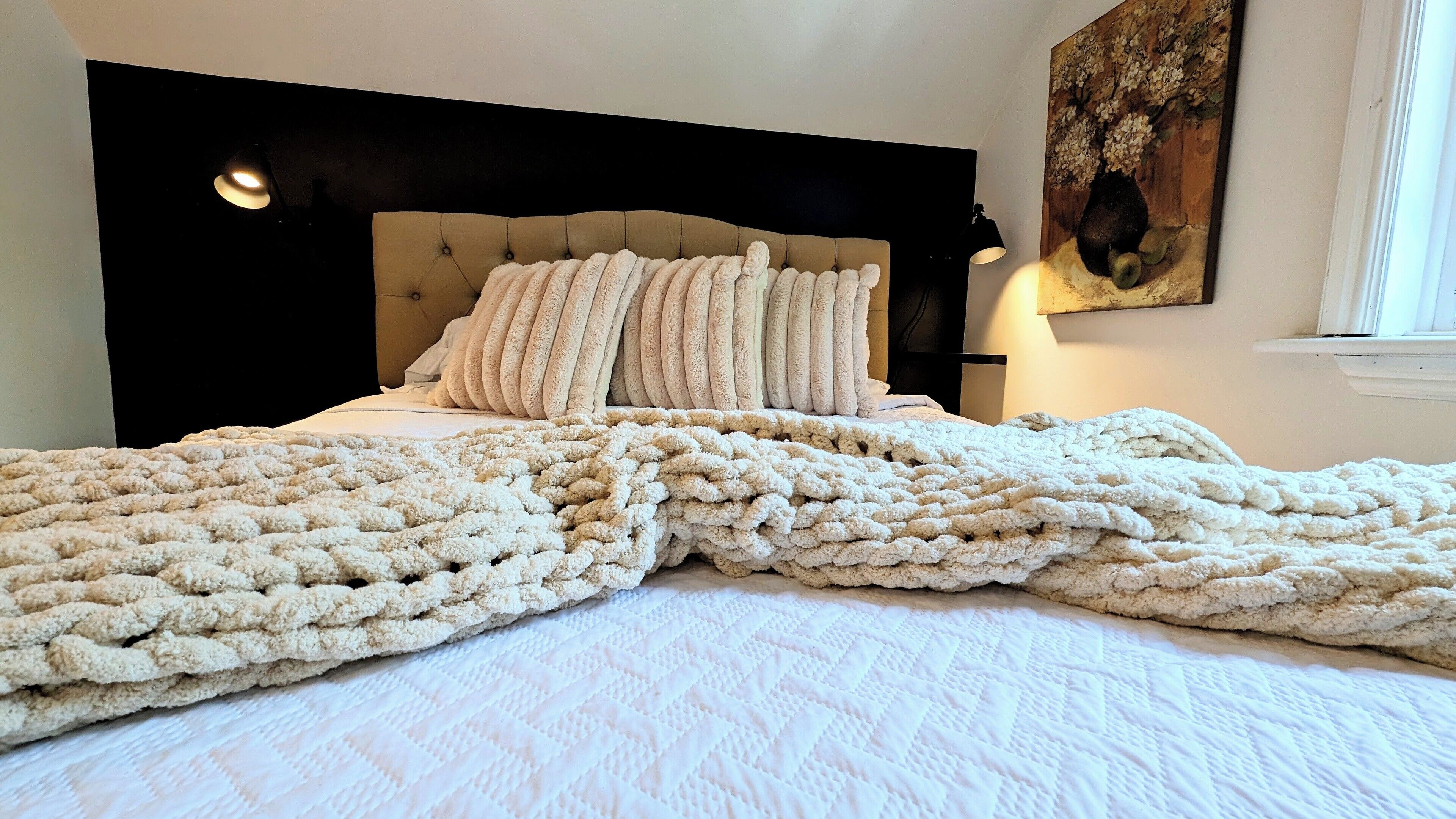 A bed with a large, textured blanket, a tufted headboard, and a painting on the wall.