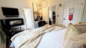 Un dormitorio con cama, televisión, silla, perchero y puerta.