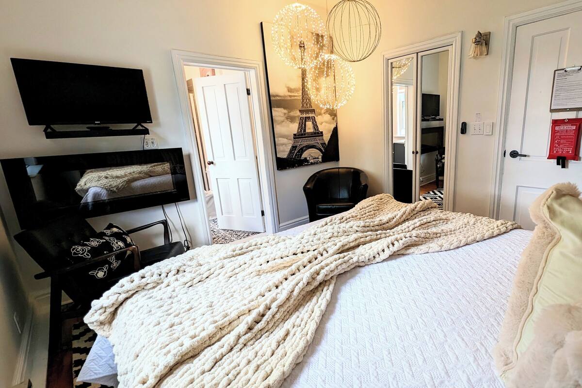 A bedroom with a bed, a television, a chair, a coat rack, and a door.