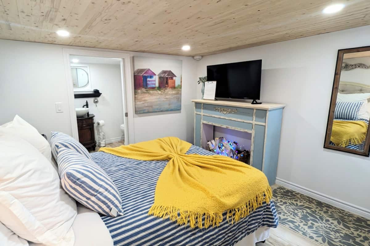A bedroom with a bed, a television, a mirror, and a painting on the wall.