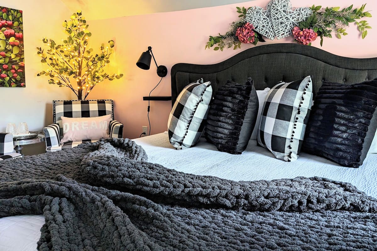 A bedroom with a bed, a nightstand, a lamp, a decorative wall piece, and a potted plant.