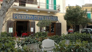 Ein Café mit Außenbereich, einer Holztür und einem Balkon mit grünen Fensterläden.