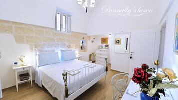 Ein Schlafzimmer mit einem Bett, Nachttischen, einem Schminktisch, einer Chandelier und einer Vase mit Blumen.
