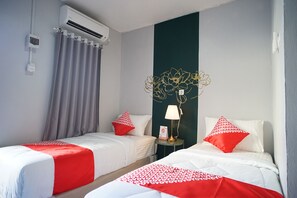 Une chambre d’hôtel avec deux lits, chacun agrémenté de draps blancs et de touches de couleur rouge, un climatiseur fixé au mur, une petite table avec une lampe et un élément décoratif mural.