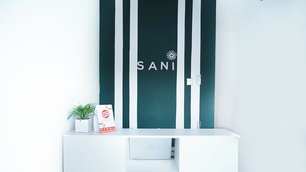 A white console with a potted plant and a box, against a wall with vertical stripes and the word "SANI" visible. - OYO 1125 Sani Guest House (Balikpapan)