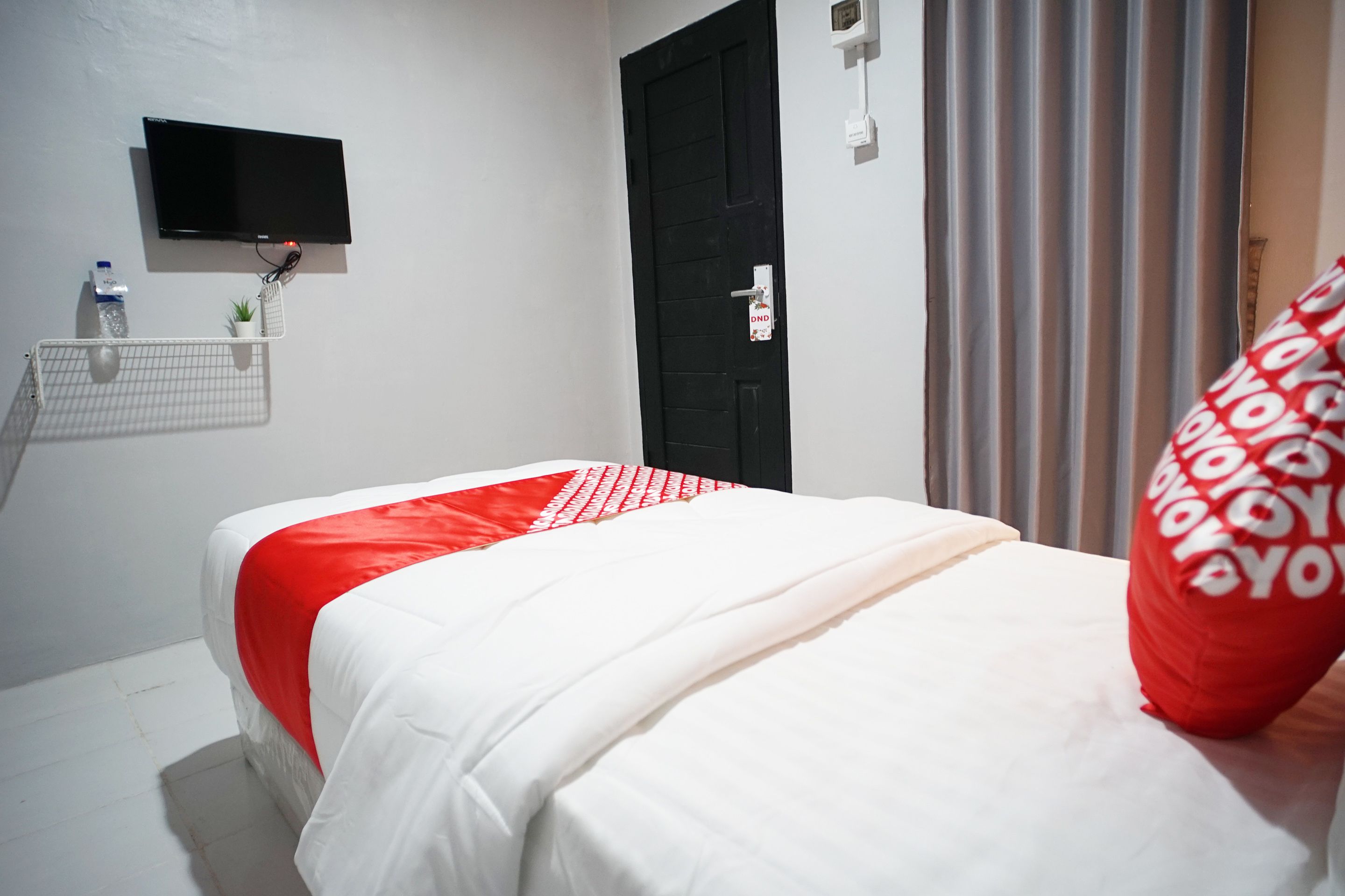 A hotel room with a bed, a mounted TV, a door with a lock, and a window with curtains.