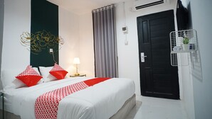 A hotel room with a bed, a bedside table with a lamp, a wall-mounted TV, a black door, and a window with curtains. - OYO 1125 Sani Guest House (Balikpapan)
