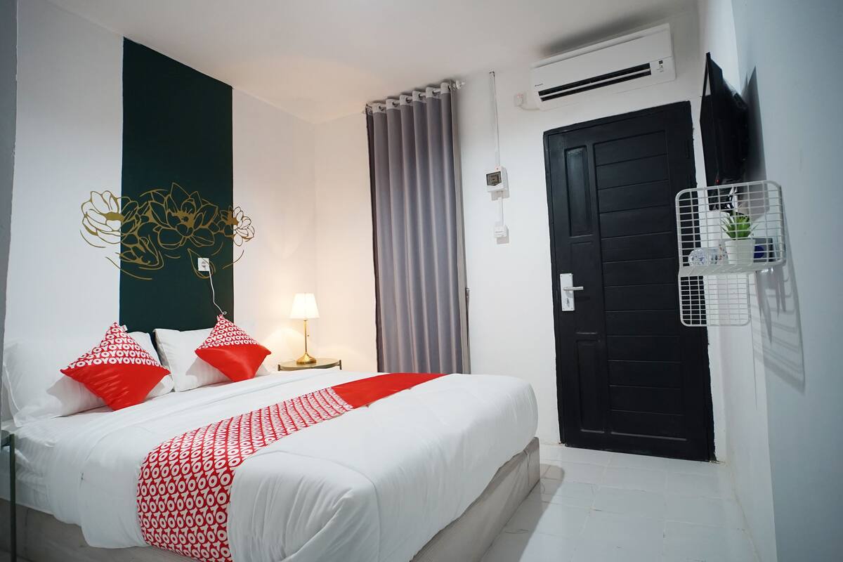 A hotel room with a bed, a bedside table with a lamp, a wall-mounted TV, a black door, and a window with curtains.