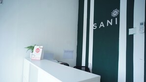 A reception desk with a white counter, a potted plant, and a bulletin board. - OYO 1125 Sani Guest House (Balikpapan)