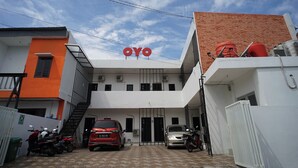 A building with a prominent 'OYO' sign, a gated entrance, and parked vehicles including a red car and motorcycles. - OYO 1125 Sani Guest House (Balikpapan)