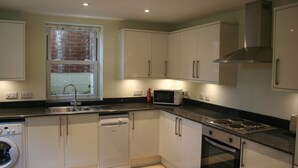 A compact kitchen with white cabinets, a built-in dishwasher, a microwave, a stove, and a window with a brick wall view.