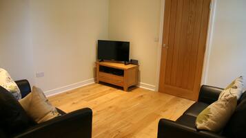 A living room with a wooden floor, a television on a wooden stand, and a door in the background.