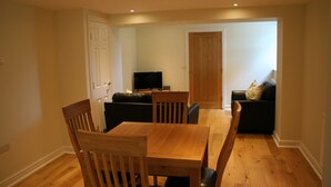 A dining area with a wooden table and chairs, a black sofa, and a television in the background.