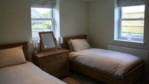A bedroom with two beds, a dresser, a mirror, and two windows with curtains.