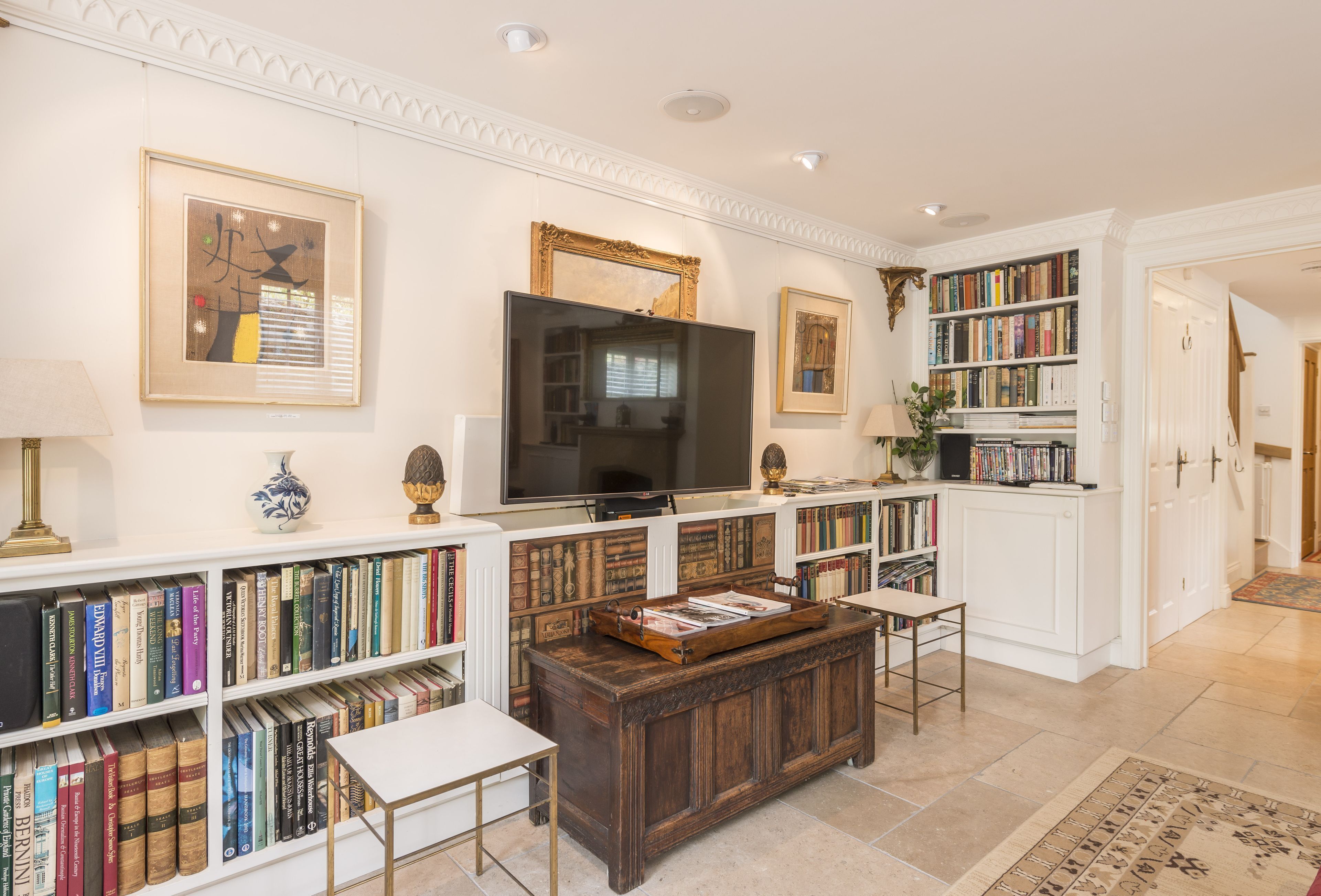 A well-lit living room with a large flat-screen TV, wooden bookshelves, a coffee table, and a white sofa.