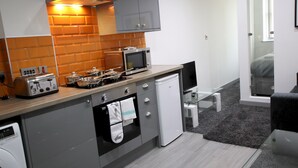 A compact kitchen with a microwave, toaster, and oven, a small sink, and a glass door leading to a bedroom.
