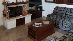 Uma sala de estar com televisão, móveis de madeira, estante de livros e uma roda de navio decorativa.