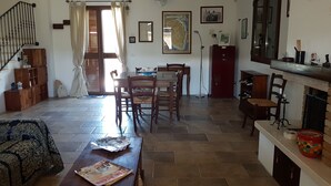 Uma área de refeições com mesa e cadeiras de madeira, bancada de cozinha com uma panela vermelha e escada com corrimão preto.