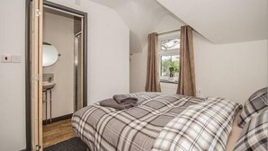 A bedroom with a bed, a bathroom with a sink, and a window with curtains. - Feather Bed Cottage B&B (Coventry)