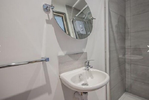 Un baño con lavamanos blanco, espejo y cabina de ducha.