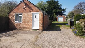 A small brick house with a white door and windows, a gravel driveway, and a garage in the background. - Feather Bed Cottage B&B (Coventry)